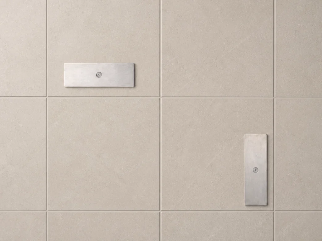 Två rektangulära adapterplattor placerade vågrätt och lodrätt på en kakelvägg.