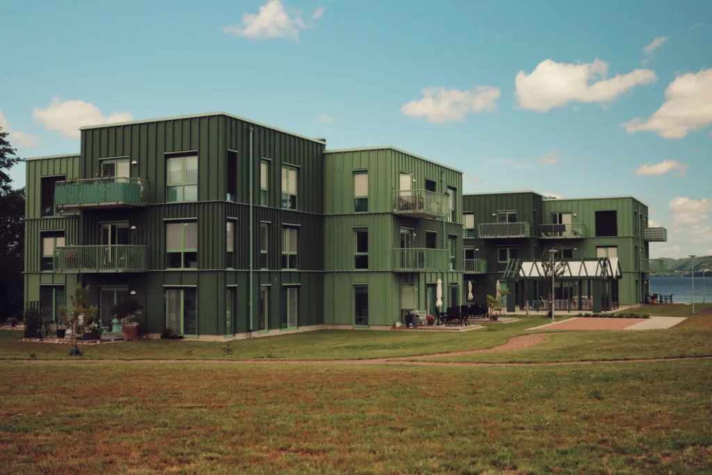 Flerbostadshus med gröna fasader, balkonger och gemensamma gräsytor nära vatten.