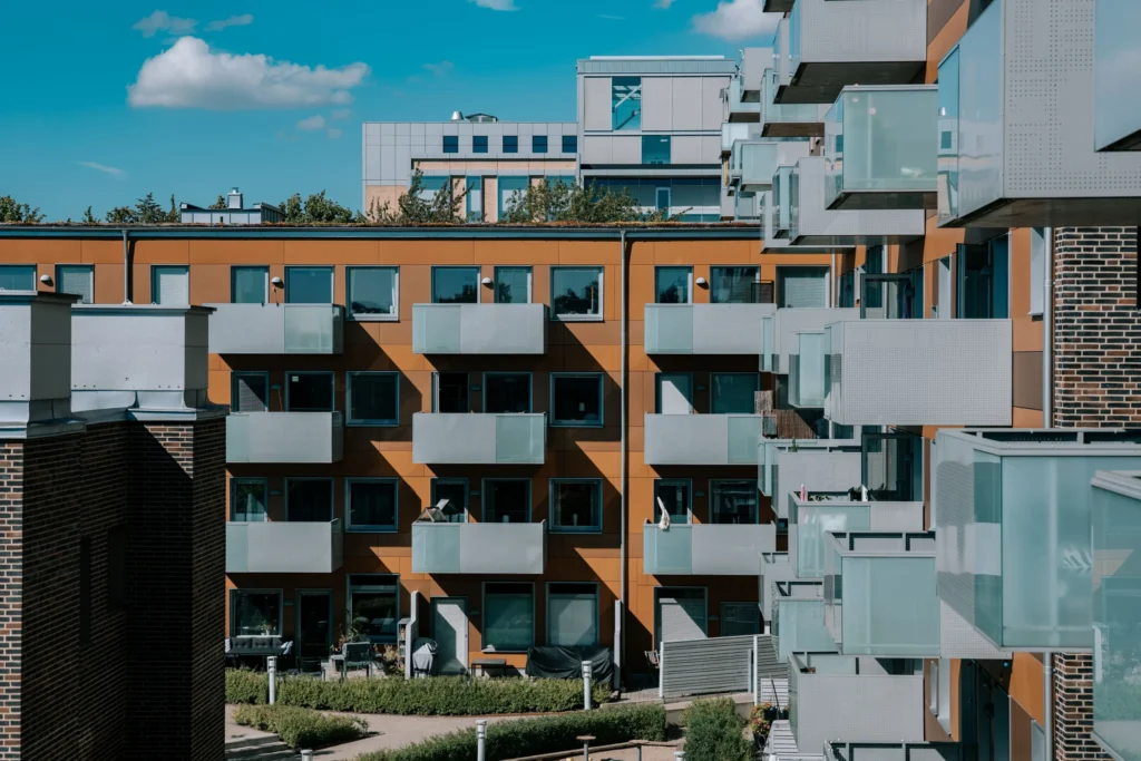 Flerbostadshus med orange fasad, ljusa balkonger och en grön innergård.